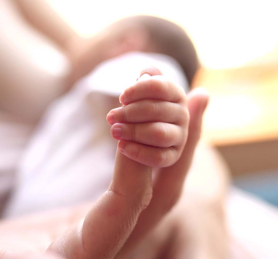 This is a soft-focus close-up image of a newborn's hand holding its mother's index finger.